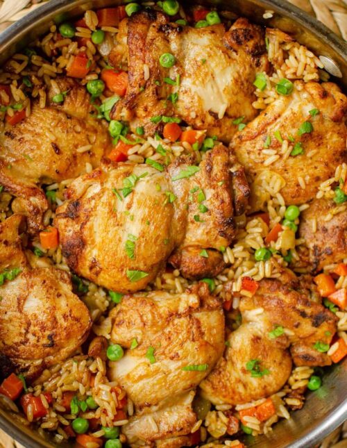 Cooked chicken and rice in a pan with parsley on top.