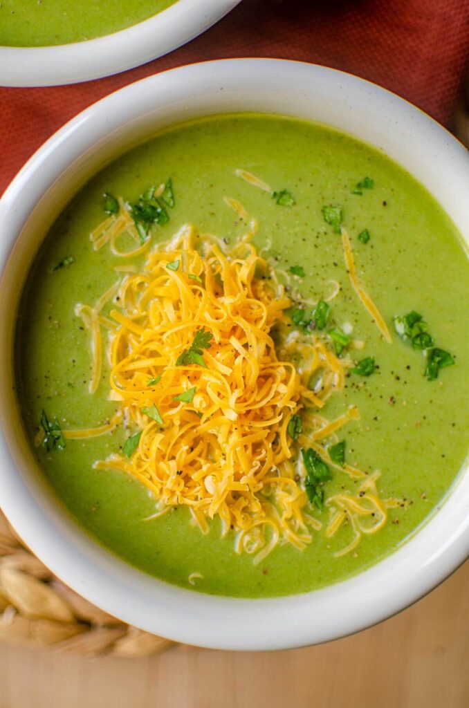 Closeup of broccoli cauliflower soup in a white bowl with cheddar cheese on top.