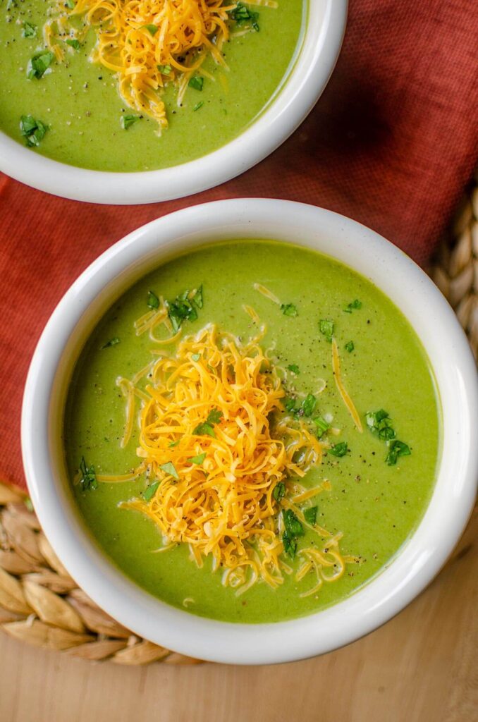 A bowl of broccoli and cauliflower soup with grated cheddar cheese and parsley sprinkled on top.