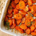 Closeup of dill carrots in a white baking dish.