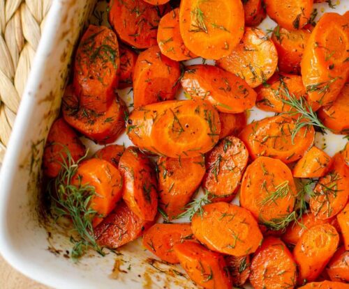 Closeup of dill carrots in a white baking dish.