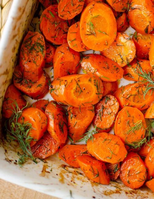 Closeup of dill carrots in a white baking dish.