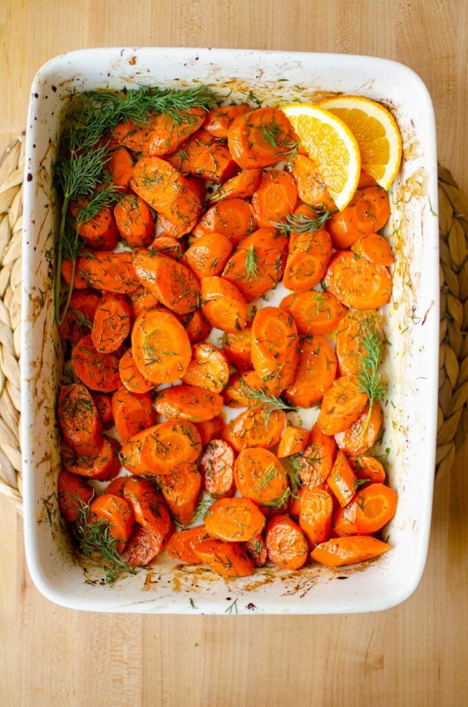 Roasted sliced carrots with dill in a white casserole dish.