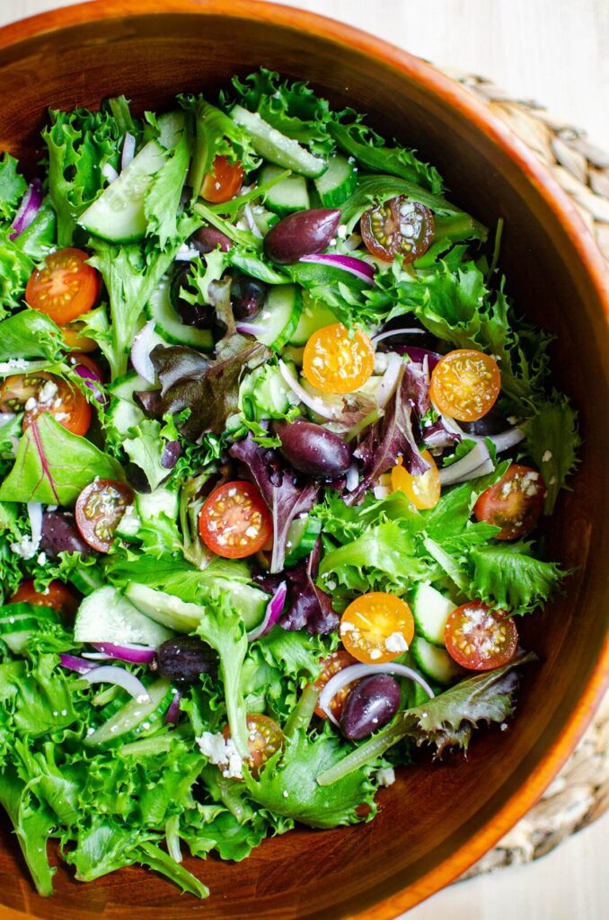 A classic salad with tomatoes, pring mix, olives and onions in a wooden salad bowl.