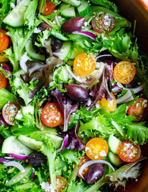 Closeup of green salad with tomatoes, red onions, feta cheese and cucumber.