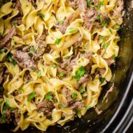 Closeup of pulled beef in the slow cooker with egg noodles with parsley sprinkled over top.