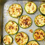 Closeup of cooked zucchini slices on a silver baking sheet.