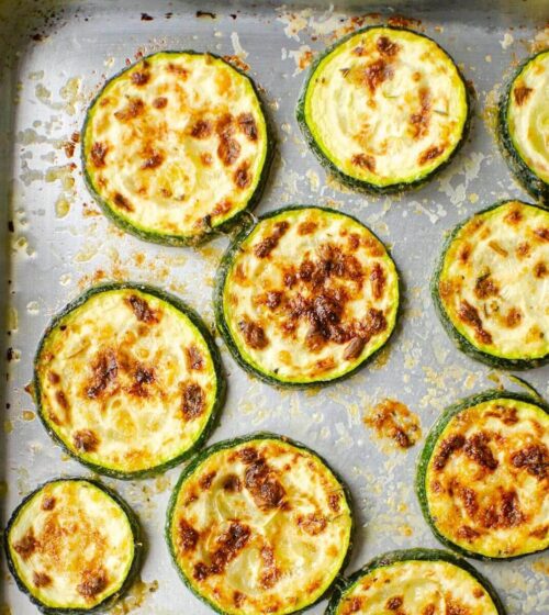 Closeup of cooked zucchini slices on a silver baking sheet.