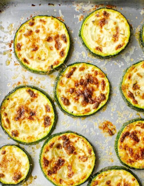 Closeup of cooked zucchini slices on a silver baking sheet.