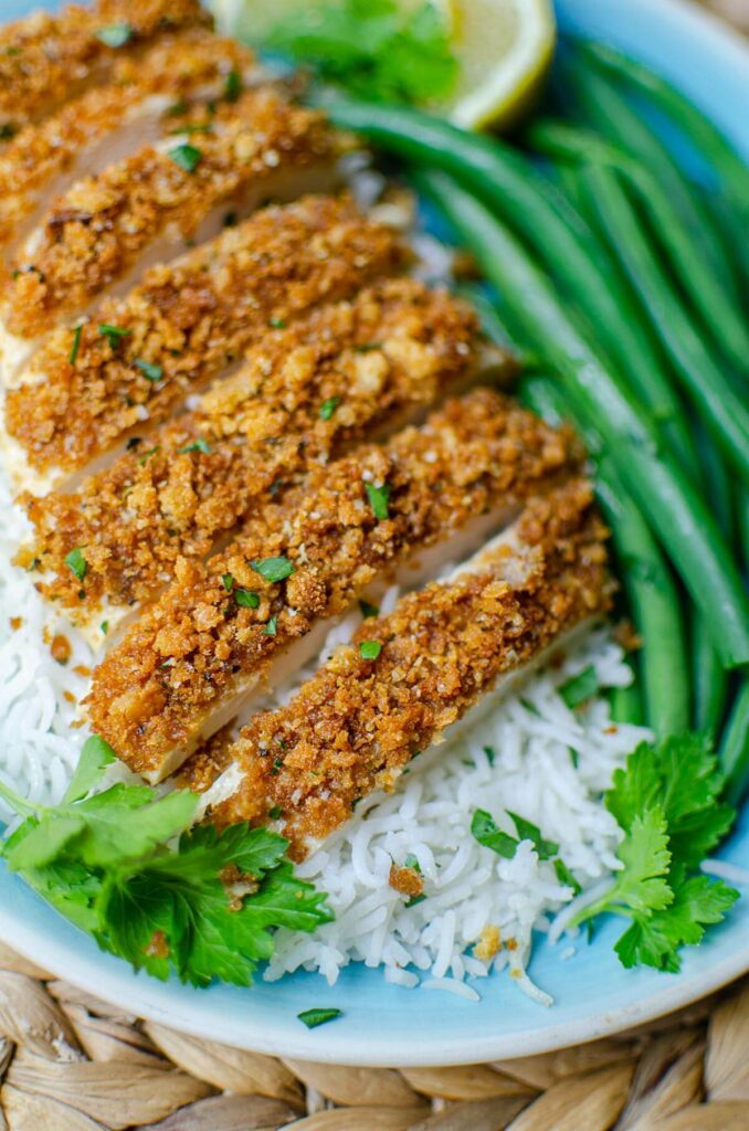 Closeup of sliced chicken on a bed of rice with green beans.