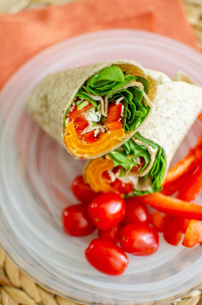 Half of a wrap on a place with cherry tomatoes and bell peppers.