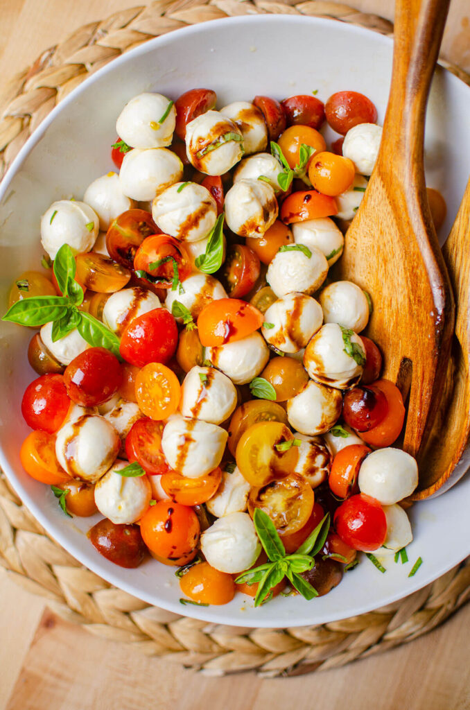 Bocconcini salad in a while bowl with a wooden spoon.
