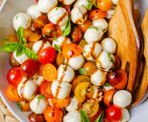 Salad in white salad bowl with wooden salad spoons.