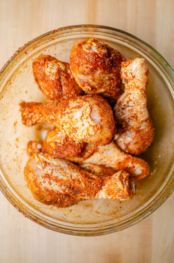 Chicken legs in a bowl coated with spice rub.