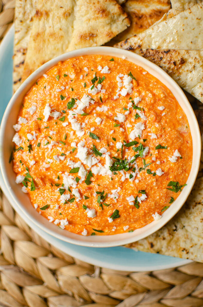 Closeup of tirokafteri in a white bowl with grilled pita on the side.