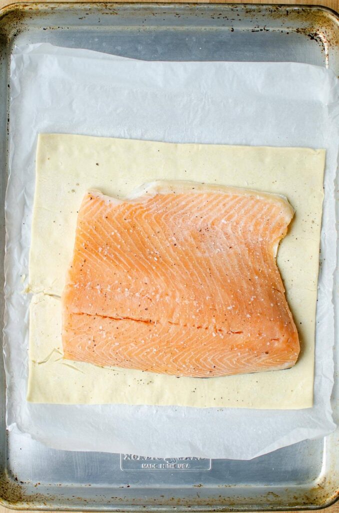 Puff pastry on parchment paper on a baking sheet, a piece of salmon is placed in the center of the puff pastry.