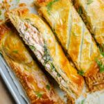 Closeup of four pieces of salmon wellington on a baking sheet.