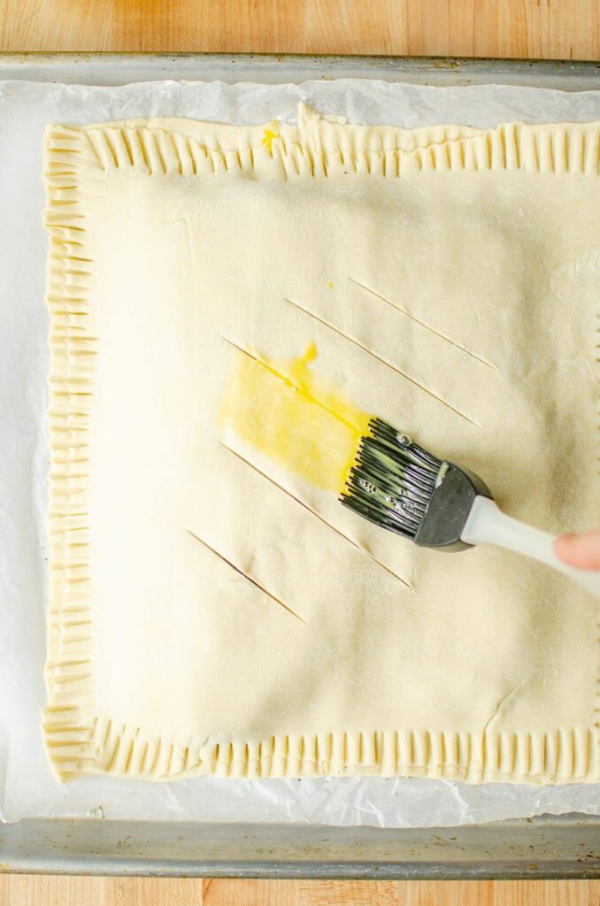 Egg being brushed overtop of puff pastry with a silicone brush.