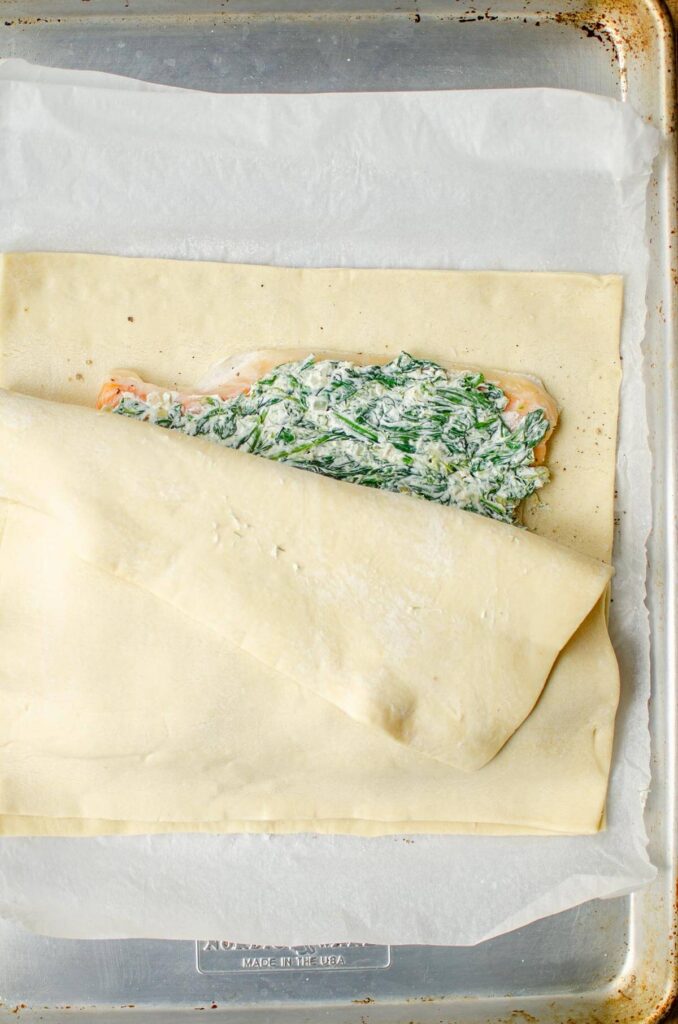 Salmon with spinach filling partially covered with a piece of puff pastry.
