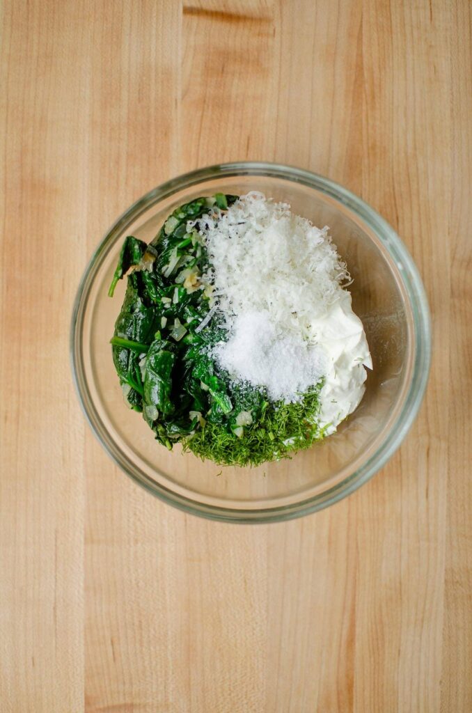 A glass bowl with cooked spinach mixture with cream cheese and parmesan cheese.