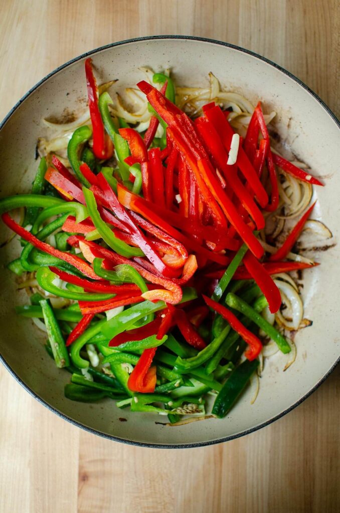 Sliced bell peppers on top of onions in braiser dish.