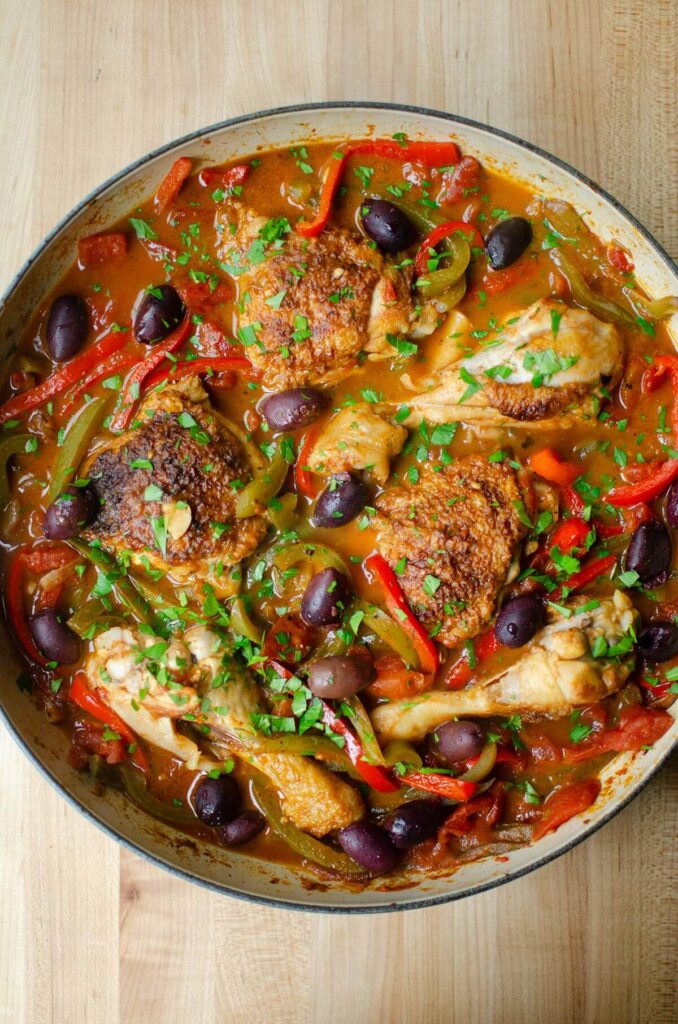Cooked chicken and peppers in braiser with olives and parsley on top.