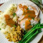 Closeup of a full plate of turkey, green beans, stuffing and mashed potatoes.