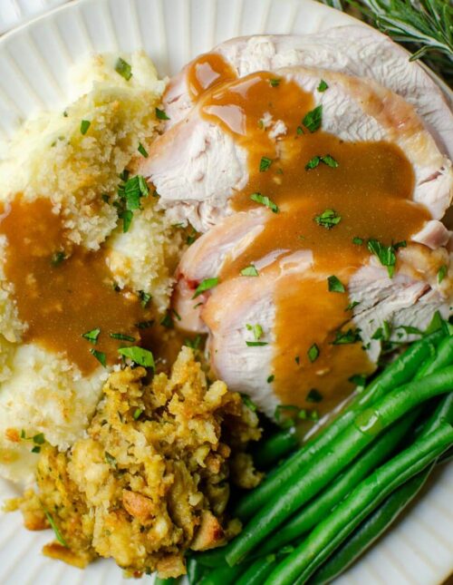Closeup of a full plate of turkey, green beans, stuffing and mashed potatoes.