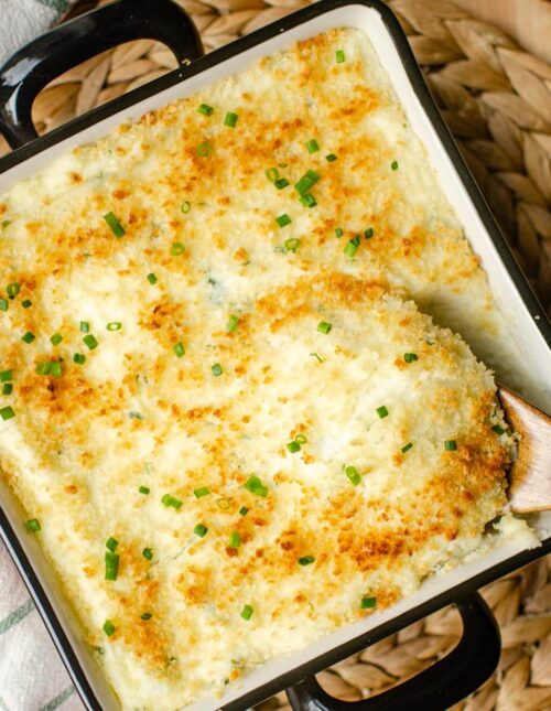 Closeup of twice baked mashed potatoes in a baking dish with a wooden spoon taking a serving.