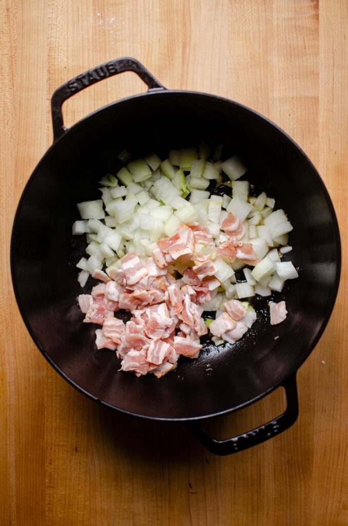 Onions and bacon sauteeing in a black Dutch oven.