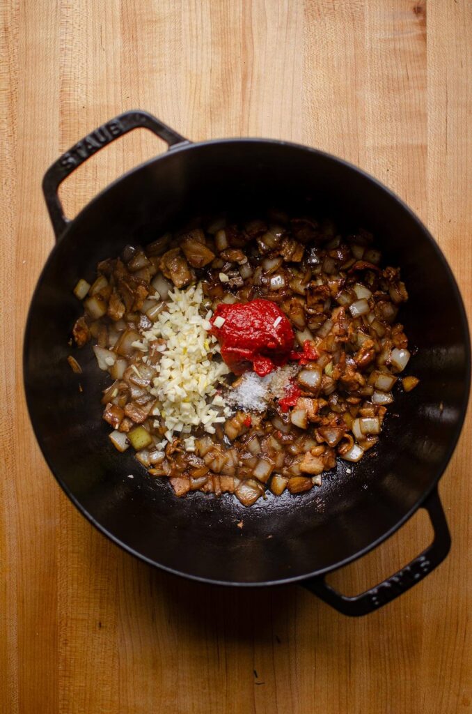 Tomato pate, garlic and salt on top of sauteed onions and bacon in a black Dutch oven.