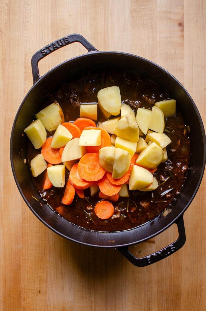 Potatoes and carrots being added to beef stew.