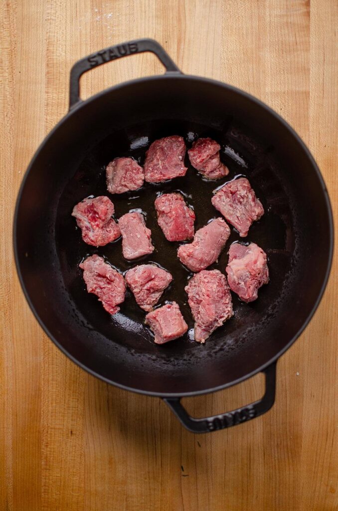 Beef cubes searing in a black Dutch oven.