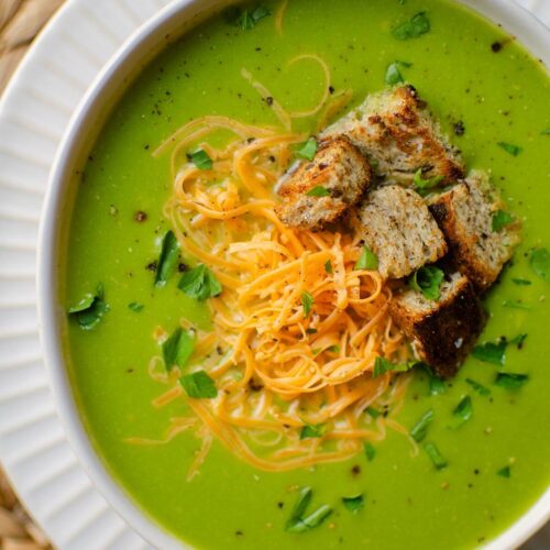 Closeup of broccolini soup in a white bowl with toppings (cheese, parsley and croutons)