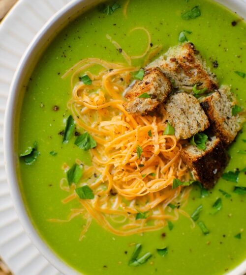 Closeup of broccolini soup in a white bowl with toppings (cheese, parsley and croutons)
