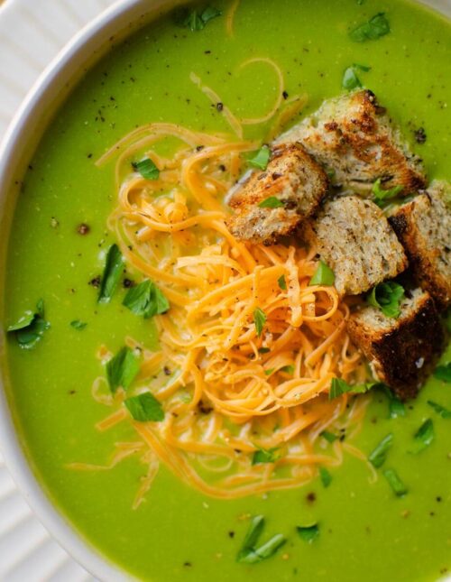 Closeup of broccolini soup in a white bowl with toppings (cheese, parsley and croutons)