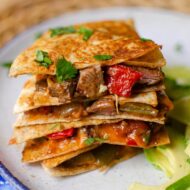 Stack of quesadillas on top of each other with sliced avocado on a plate.