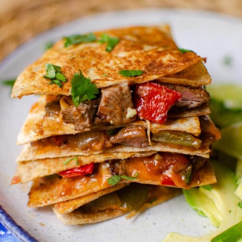 Stack of quesadillas on top of each other with sliced avocado on a plate.