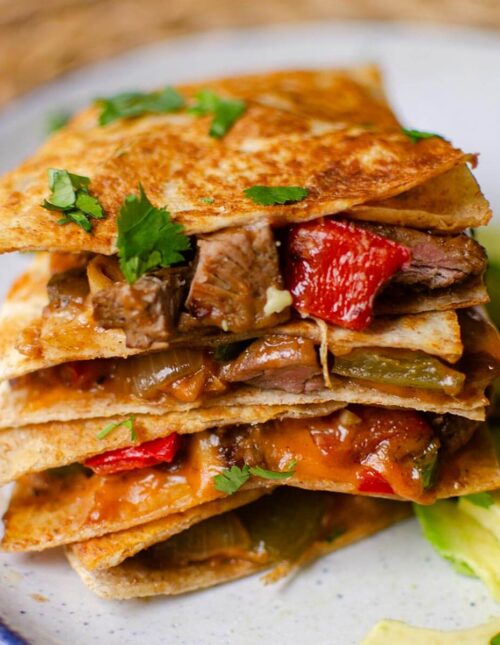 Stack of quesadillas on top of each other with sliced avocado on a plate.