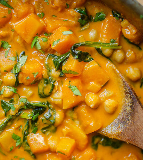 Closeup of butternut squash chickpea curry with a wooden serving spoon.