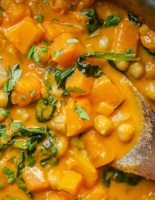 Closeup of butternut squash chickpea curry with a wooden serving spoon.