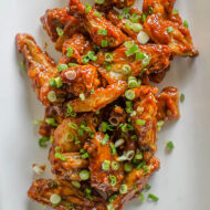 Chicken wings on a white plate with green onions on top.