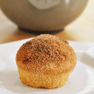 A muffin donut on a white plate with a grey bowl in the background.
